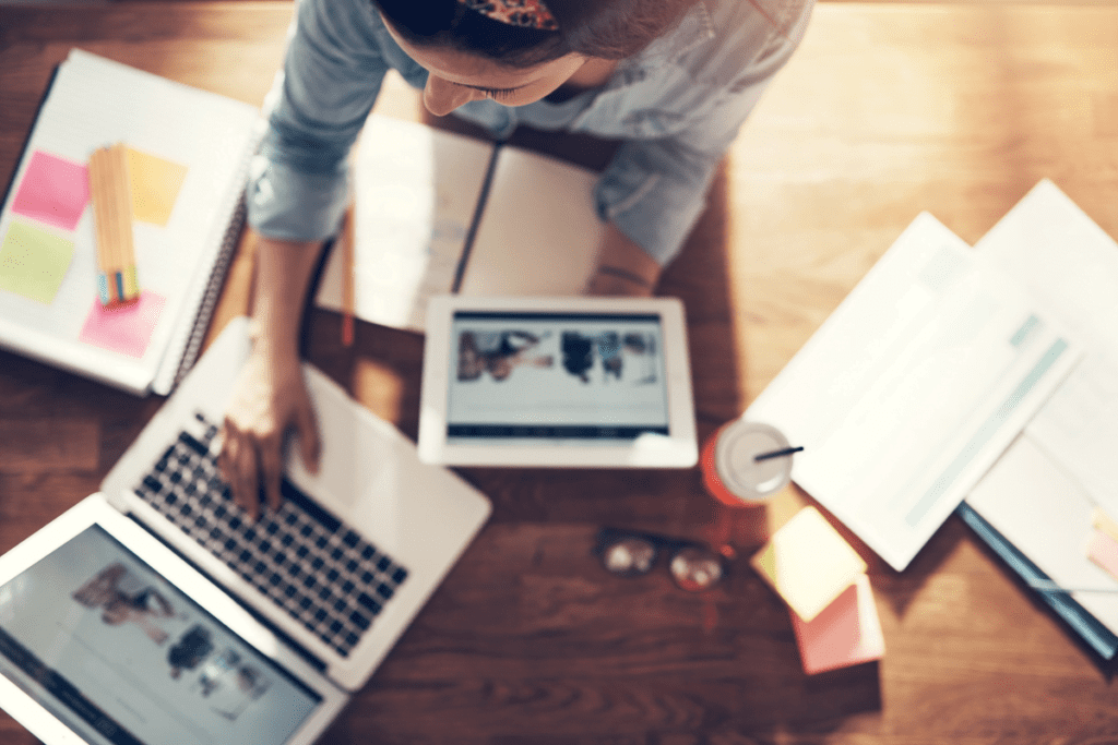 A creative business owner sit at a workspace loaded with screens and documents.