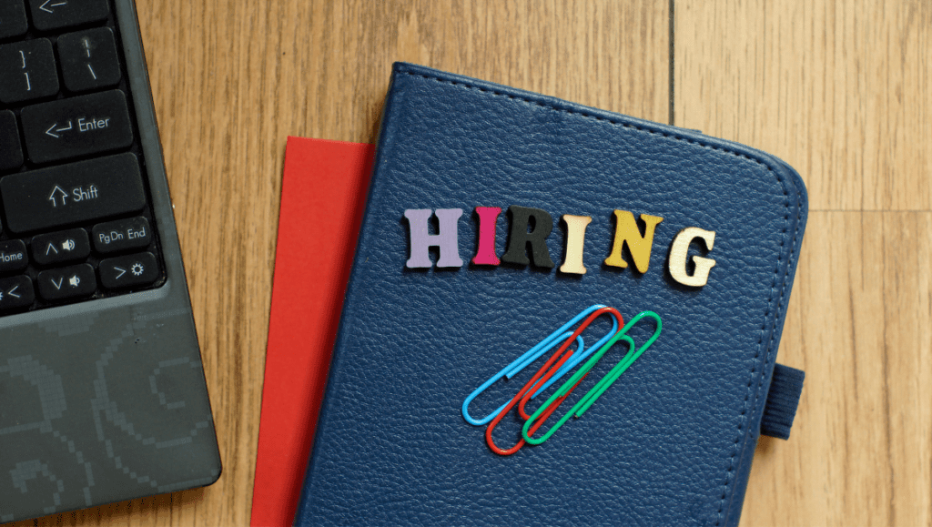 A padfolio with colorful letters spelling “Hiring” sits on a desk next to a laptop. Hiring mistakes are dangerous but avoidable for small business owners.