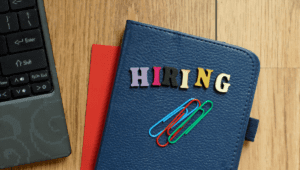A padfolio with colorful letters spelling “Hiring” sits on a desk next to a laptop. Hiring mistakes are dangerous but avoidable for small business owners.