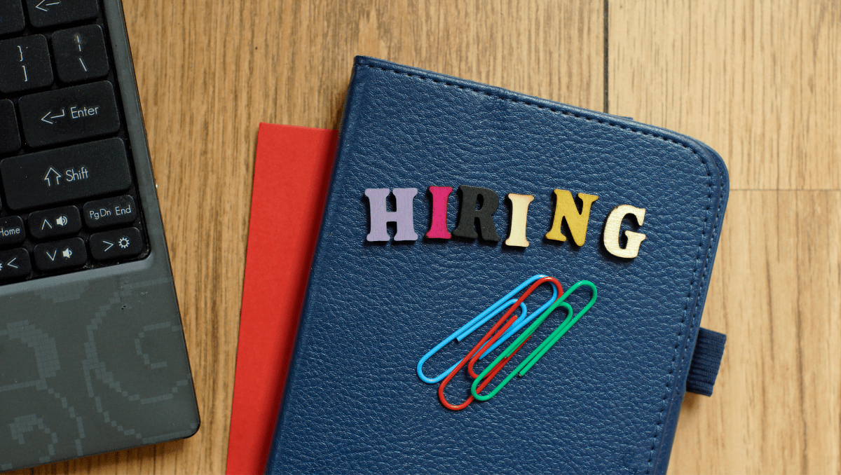 A padfolio with colorful letters spelling “Hiring” sits on a desk next to a laptop. Hiring mistakes are dangerous but avoidable for small business owners.