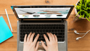 Hands type on a computer, next to which sit a notepad, headphones, and a plant. In this post, Erika Macauley sheds light on business tasks that can be automated.