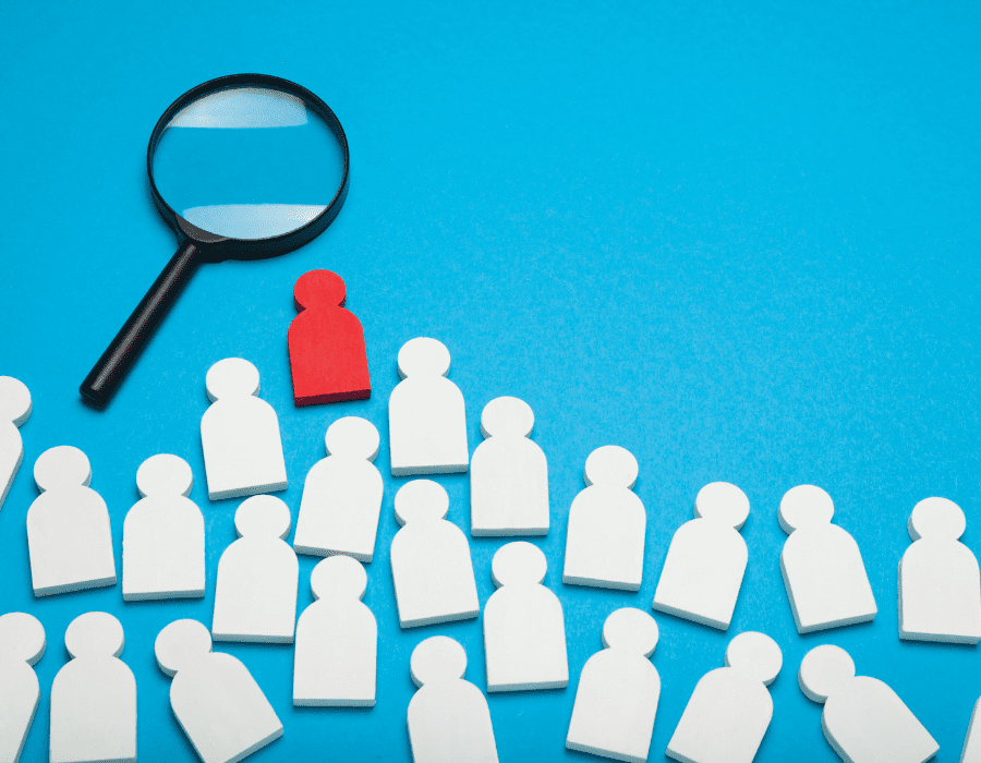 A magnifying glass looms over a sea of people cutouts, hovering over the red one that stands out against the crowd. Automating your recruiting and hiring is one of the business tasks that can be operated that simplifies and streamlines your operations.